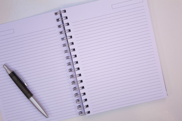 NOTEBOOK WITH BLANK PAGE AND BLACK PEN ON WHITE TABLE