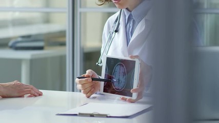 Woman doctor showing x-ray image of scull on screen of digital tablet and explaining it to senior female patient during consultation in healthcare center - Powered by Adobe