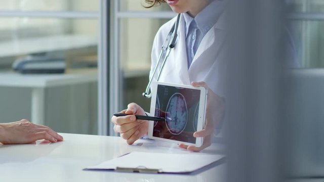 Woman doctor showing x-ray image of scull on screen of digital tablet and explaining it to senior female patient during consultation in healthcare center