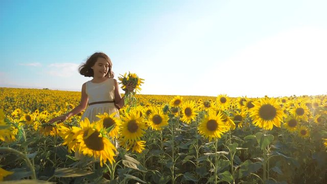 Happy little girl running lifestyle happy free across the field with sunflowers. slow motion video . smelling big sunflower on summer field. Delight of a pleasant smell. Summer holiday. concept