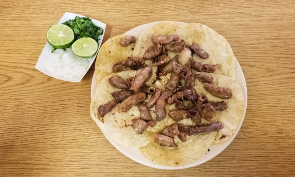 Taco de tripitas. Tortilla with beef tripe or chunchulo (chunchurria). Traditional Mexican food dish over wooden table and lemon and salt side.