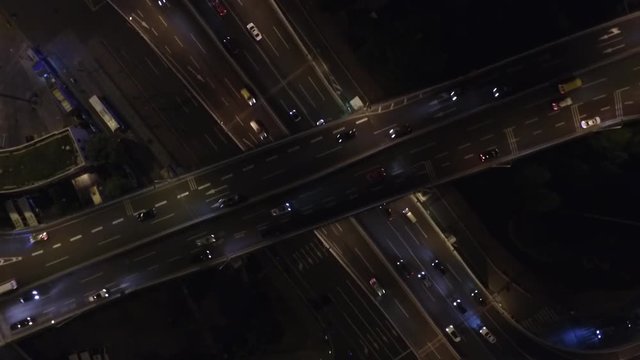 Looking down close up of highway crossover in Shanghai at night. Drone footage of downtown traffic on Chinese freeway interchange in evening.