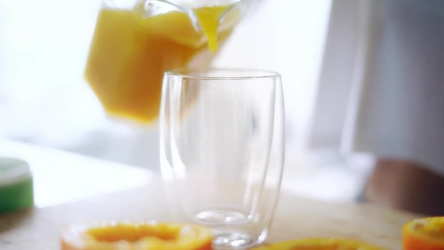 Woman pouring orange juice from glass jar into glass. Close up glass of fresh orange juice. Preparing healthy breakfast from natural ingredient. Homemade fruit juice on table. Organic vitamin drink