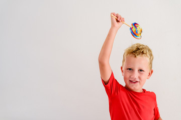 Boy with red shirt on white background eating a lollipop colorful fun and laughing.