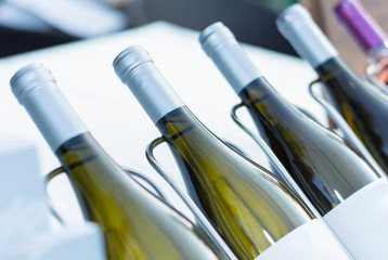 Glass bottle with white wine in row standing in metal rack on desk. Alcohol drink decoration concept. Close up, selective focus