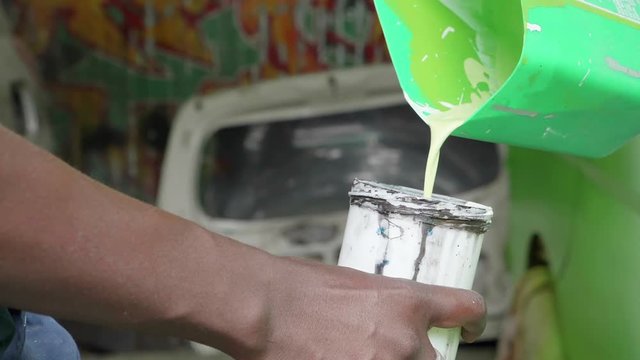 A close up of a man pouring green paint into a spray paint gun