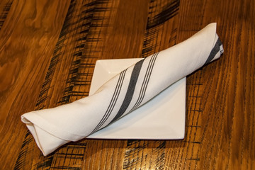 Cuttlery wrapped in a striped linnen napkin lying on a bread dish on a wooden table