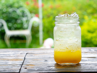 A fresh orange soda drink filled with ice in a vintage style glass container Full of ice in the glass. Placed on  wooden desk in garden with a green background
