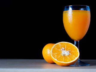 Half oranges are placed on a sack on the table, with glass of orange juice on the side on a black background, stilllife