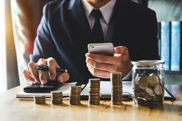 accountant working on desk in office using calculator and smartphone to calculate budget. concept finance and accounting in morning light