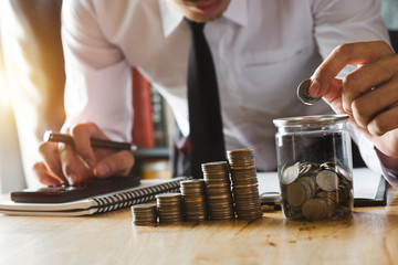 businessman holding coins putting in glass with using smartphone and calculator to calculate  concept saving money for finance accounting
