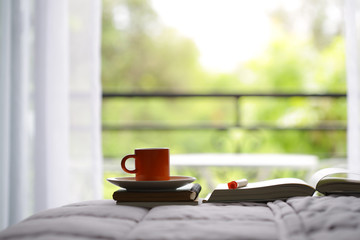 Orange cup and notebooks on bed with windows view