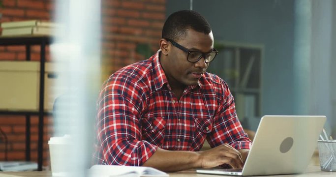 Young African American man office manager sitting at the computer in his office and failing his work, being dissapointed and upset.