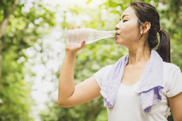 Asian woman drinking water in bottle at the park after doing sport outdoors 