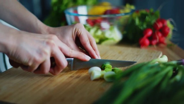 Woman hands cutting green onion for salad. Close up fresh vegetables cooking ingredients on kitchen table. Housewife preparing healthy breakfast at home. Vegetarian food cooking on wooden board