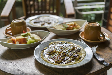 breakfast table setting with banana omelet and fresh mixed fruit salad, with coffee or tea cups in bali homestay