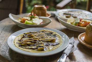 breakfast table setting with banana omelet and fresh mixed fruit salad, with coffee or tea cups in bali homestay