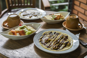 breakfast table setting with banana omelet and fresh mixed fruit salad, with coffee or tea cups in bali homestay