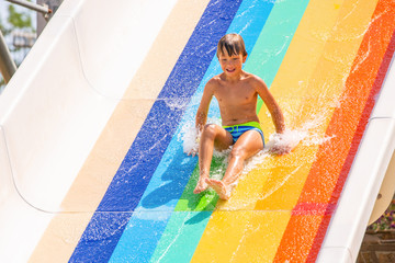 A happy boy on water slide in a swimming pool having fun during summer vacation in a beautiful aqua...
