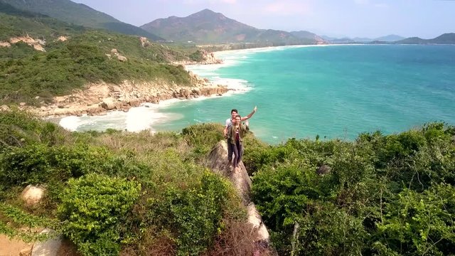 couple stands at edge of precipice waves hands against seascape