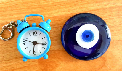 evil eye amulet and blue alarm clock, small, key chain on wood background