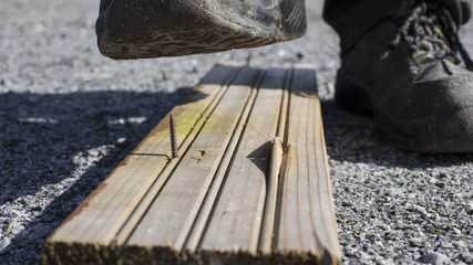The builder is entering a sharp screw in Finland. At the foot he has a safety shoe. The focus point is on the nail.
