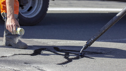 Workers repair the road, pour small cracks with bitumen to prevent further destruction of the road surface