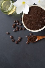 coffee ground scrub with beans, oil and plumeria flowers on black board background, beauty spa concept 