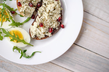 Cheese, arugula and garnet grains sandwich on a light wooden background