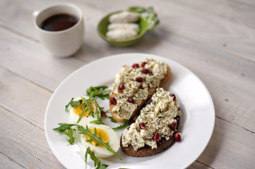 Cheese, arugula and garnet grains sandwich on a light wooden background