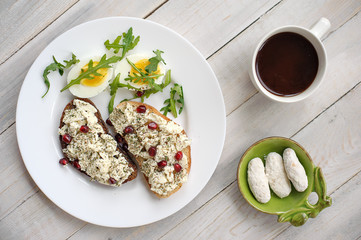 Cheese, arugula and garnet grains sandwich on a light wooden background
