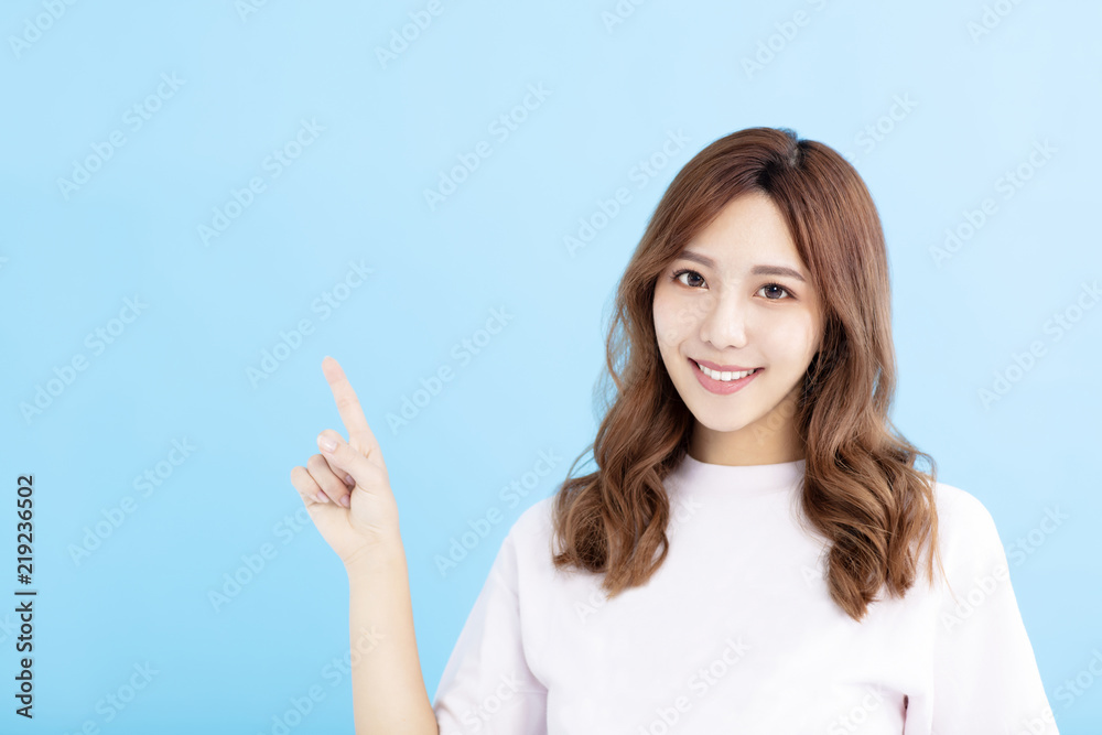 Wall mural smiling young woman pointing at blue background