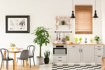 Real photo of bright kitchen interior with checkerboard floor, pastel pink accessories, fresh...