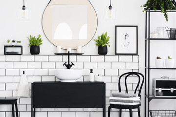 Real photo of black and white bathroom interior with a mirror, cupboard, chair and plants