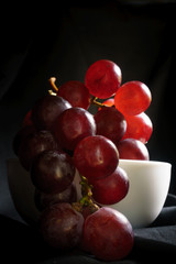 Red grapes in the dark, red grapes in a white bowl in the dark corner