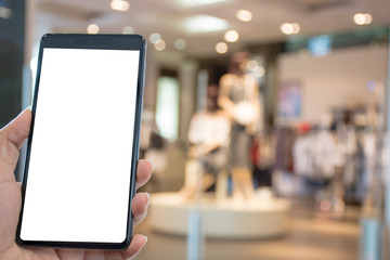 Female hand holding and showing mobile smartphone with blank white screen with boutique shop and model blurred background.