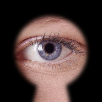 close-up of human female blue eye looking through keyhole