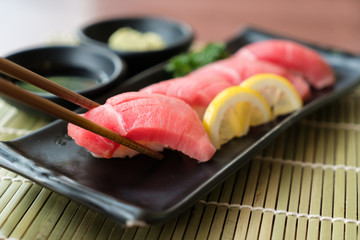 Otoro tuna sushi on black plate along with Japanese sauce and green leaf decoration, Japanese food, close up at sushi ..
