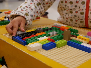 Fototapeta premium Hands of a baby playing colorful interlocking plastic bricks - child development through playing toys