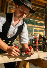 Carpenter in seiner Kluft und Schlapphut,  bearbeitet mit Hobel Holzbalken