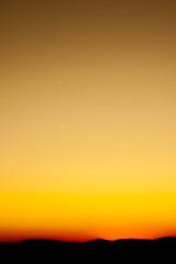 An orange sunset or sunrise shot on portrait orientation. Background wallpaper photo for a smartphone. Orange and yellow sky, mountain landscape on horizont.