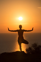 Fototapeta premium silhouette of a woman doing yoga during the sunset 