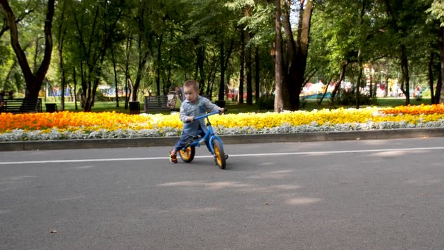 Slow motion 4k. A child rides a running bike in the Park. A little boy rides a balance bike in a city public Park.