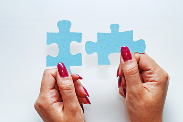 Female hands hold two elements of a puzzle piece on a white background.