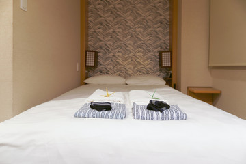 Nightgowns and towel on white bed in Japanese hotel room.