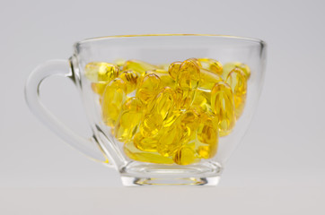 Golden color fish oil supplement in soft gel capsule in clear glass, healthy product.