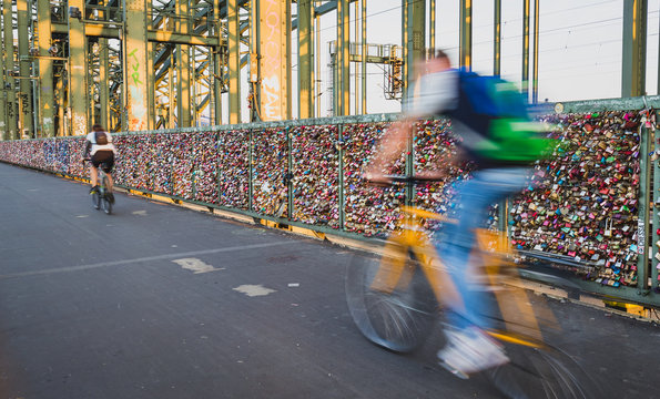 Motion blurred cyclists passing walls of padlocks on the Hohenzollernbr&uuml;cke (Hohenzollern Bridge) in Cologne, Germany