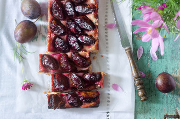 Sweet pie from short pastry with caramelized plums and ripe plums on a wooden table. Rustic style.