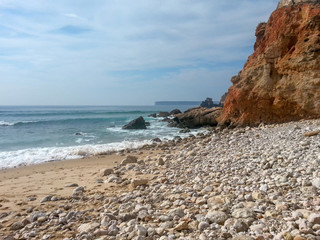 Beautiful beach with pebbles and big orange rock 