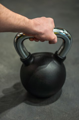 Naklejka na ściany i meble health and sport lifestyle concept, a man holds a black metal kettlebell weight in a rubber sheath